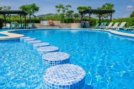 A swimming pool with clear blue water, a lifebuoy, and lounge chairs.