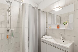 A modern bathroom with a shower, a sink, a mirror, and a shelf with toiletries. - Villa 'Artemis' with Sea View, Wi-Fi, and Air Conditioning in Grimaud (Grimaud)