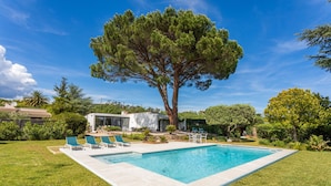 A swimming pool with a tree in the background, a small building, and a grassy area with lounge chairs. - Villa 'Artemis' with Sea View, Wi-Fi, and Air Conditioning in Grimaud (Grimaud)