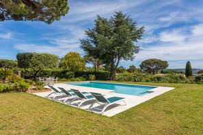 A rectangular swimming pool with a tiled deck, surrounded by a well-maintained lawn and various trees. - Villa 'Artemis' with Sea View, Wi-Fi, and Air Conditioning in Grimaud (Grimaud)