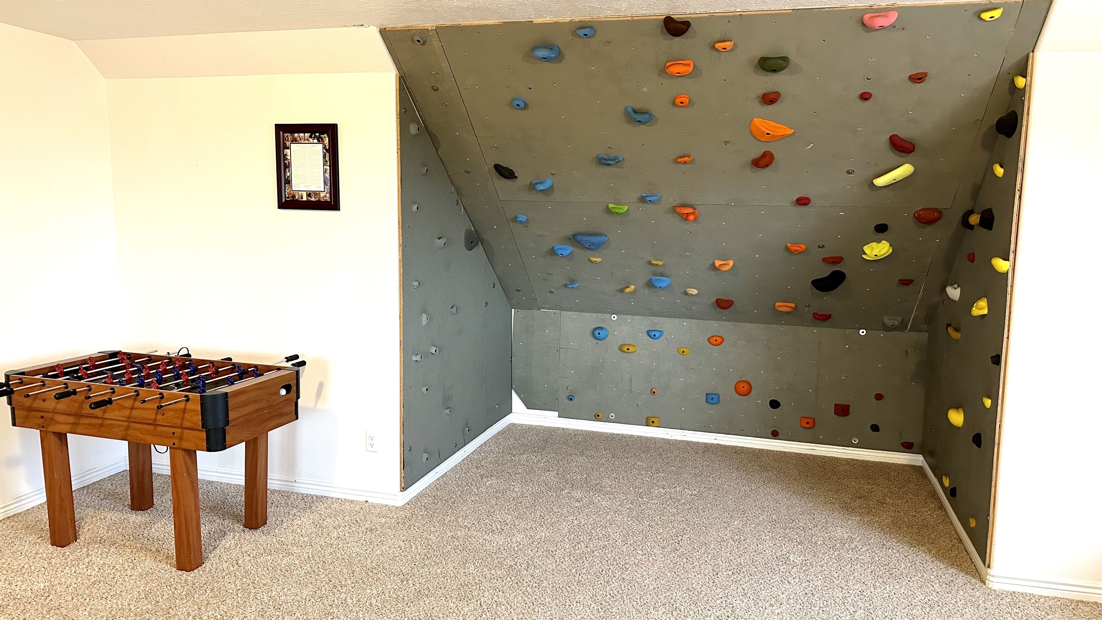 Ein Zimmer mit Kletterwand, Kicker und einem gerahmten Zertifikat an der Wand.