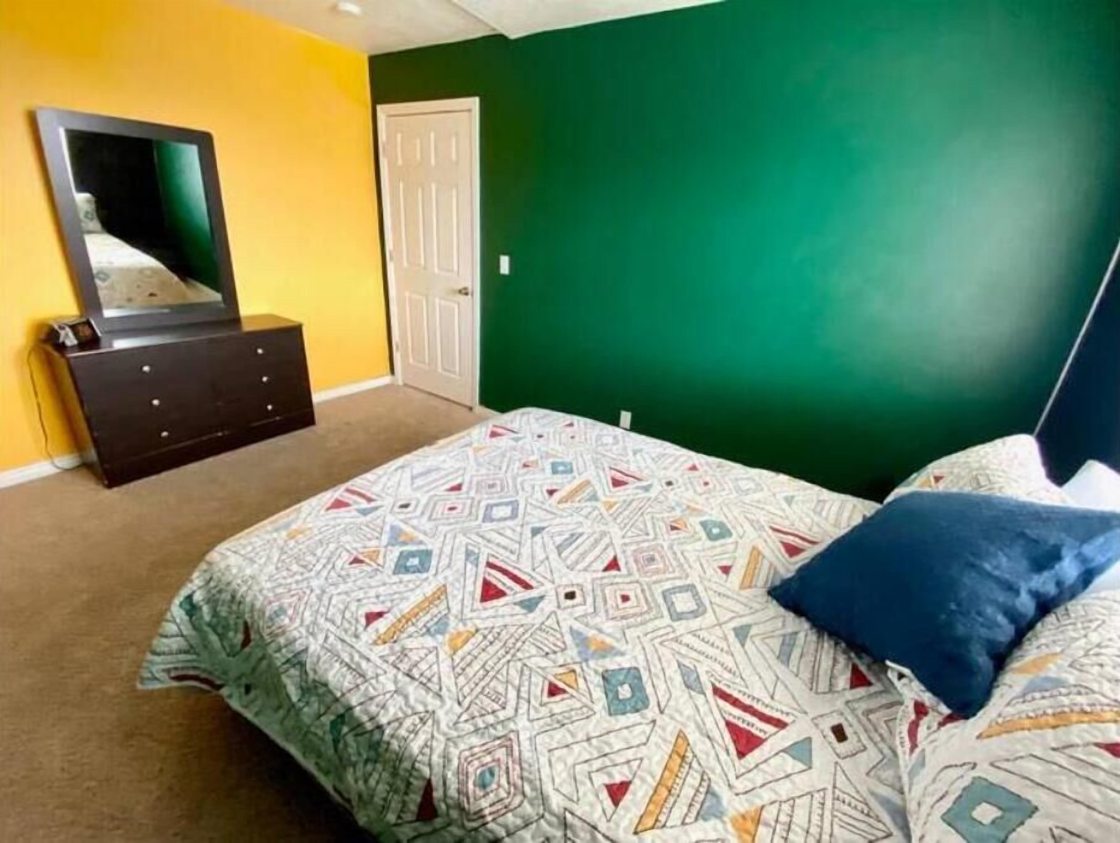 Een slaapkamer met een bed, een dressoir, een spiegel en een deur.