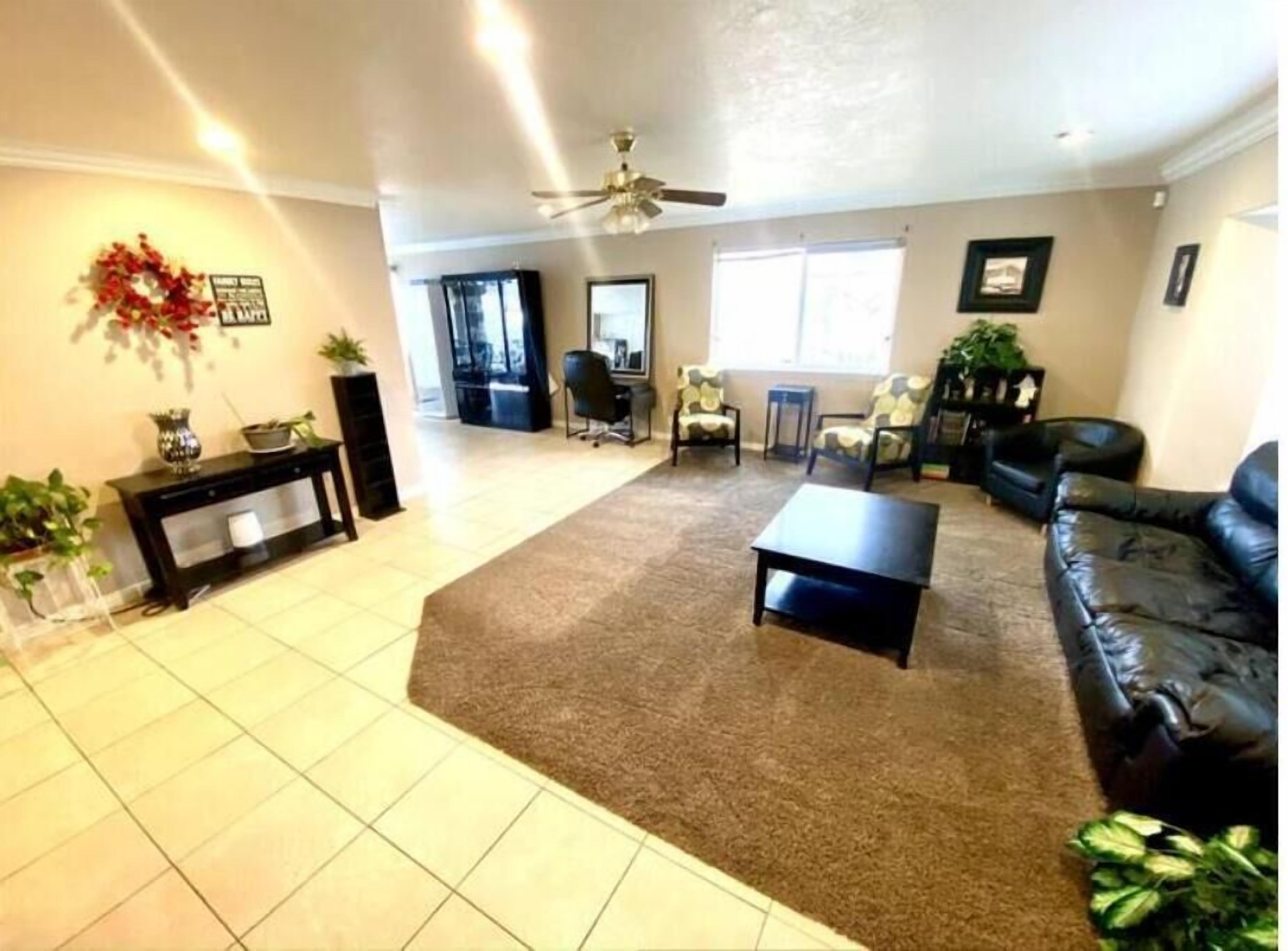 A spacious living room with a large brown carpet, a black sofa, a coffee table, and a ceiling fan.