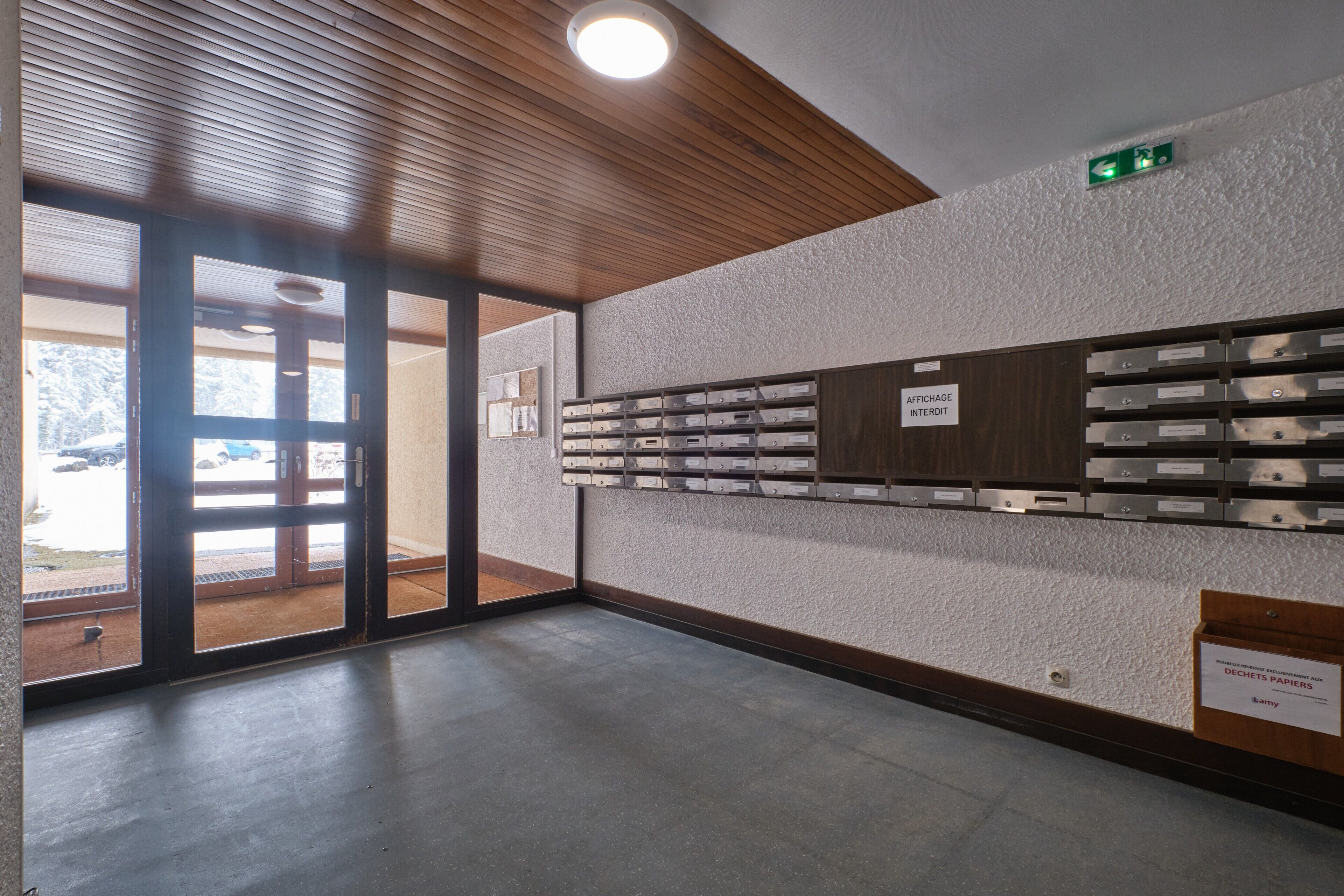 Ein Empfangsbereich mit Holzboden, einem an der Wand befestigten Briefkasten und einer Tür, die nach draußen führt.