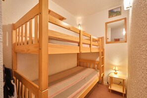 Una cama individual superpuesta con una mesita de noche pequeña y una lámpara, un espejo en la pared y una puerta con perchero.