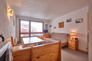 Una habitación con una mesa de comedor de madera, sillas, un sofá, un mueble bajo y un ventanal con vistas a edificios.