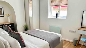 A modern bedroom with a bed, bedside table, mirror, window, and a small desk area. - Charming Period Apartment, Near Uni & Hospital, Parking (Reading)