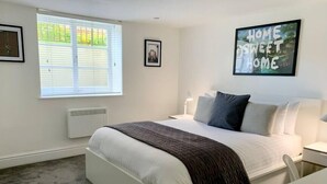 A bedroom with a bed, a bedside table, a chair, a window with blinds, a radiator, and a framed picture on the wall. - Period Apartment for 3, Near Uni & Hospital, Parking (Reading)