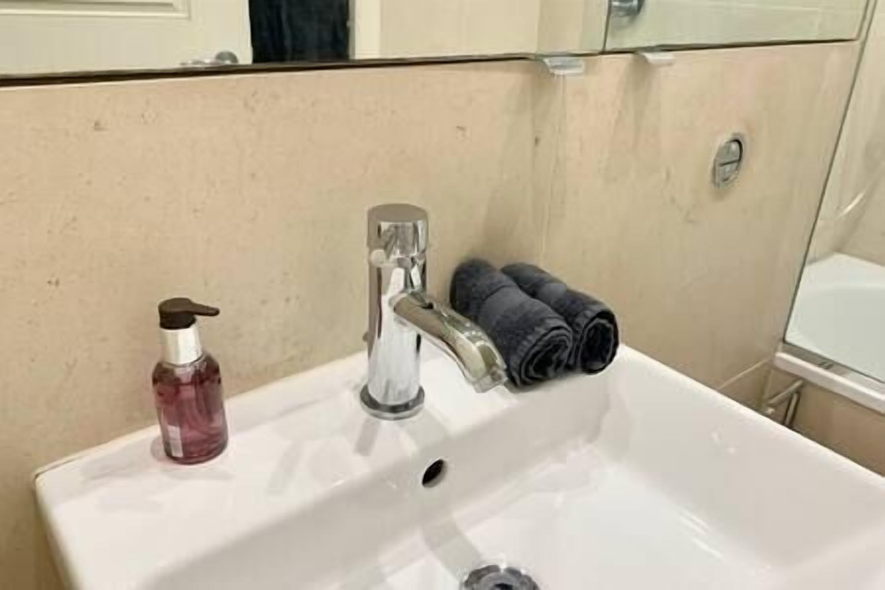 Een badkamermeubel met een zeepdispenser, een kraan en een handdoekhouder met opgerolde handdoeken.