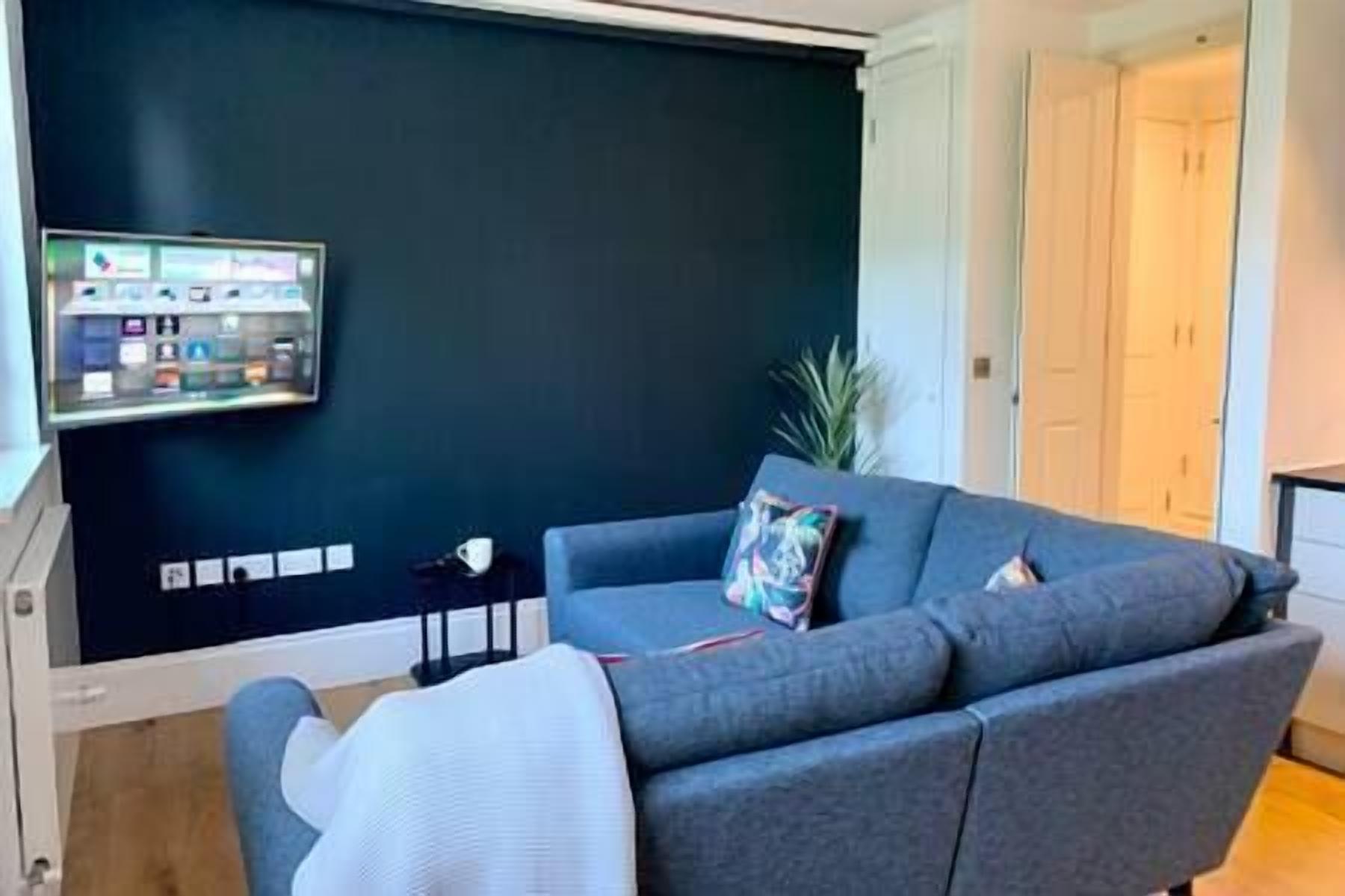 A living room with a dark blue wall, a grey sofa, a small side table, and a plant.