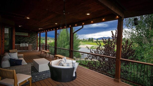 A covered outdoor area with a wooden deck, wicker furniture, and a view of a river and mountains. - Casa Del Rio hot tub, sauna, movie theater #020796 (Buena Vista)