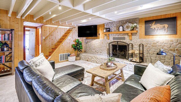 A cozy living room with a fireplace, leather sofas, a coffee table, and a bookshelf. - Solitude Mountain Cabin: Creek-Side View & Hot Tub (Brighton)