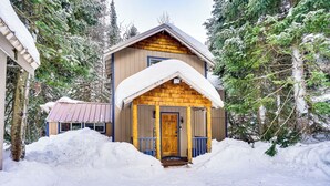 A cabin with a wooden exterior and a snow-covered porch, surrounded by snow and trees. - Solitude Mountain Cabin: Creek-Side View & Hot Tub (Brighton)