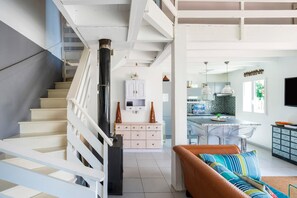 Un escalier mène à un espace de vie comprenant un canapé, une cuisine avec des tabourets de bar et une table à manger.