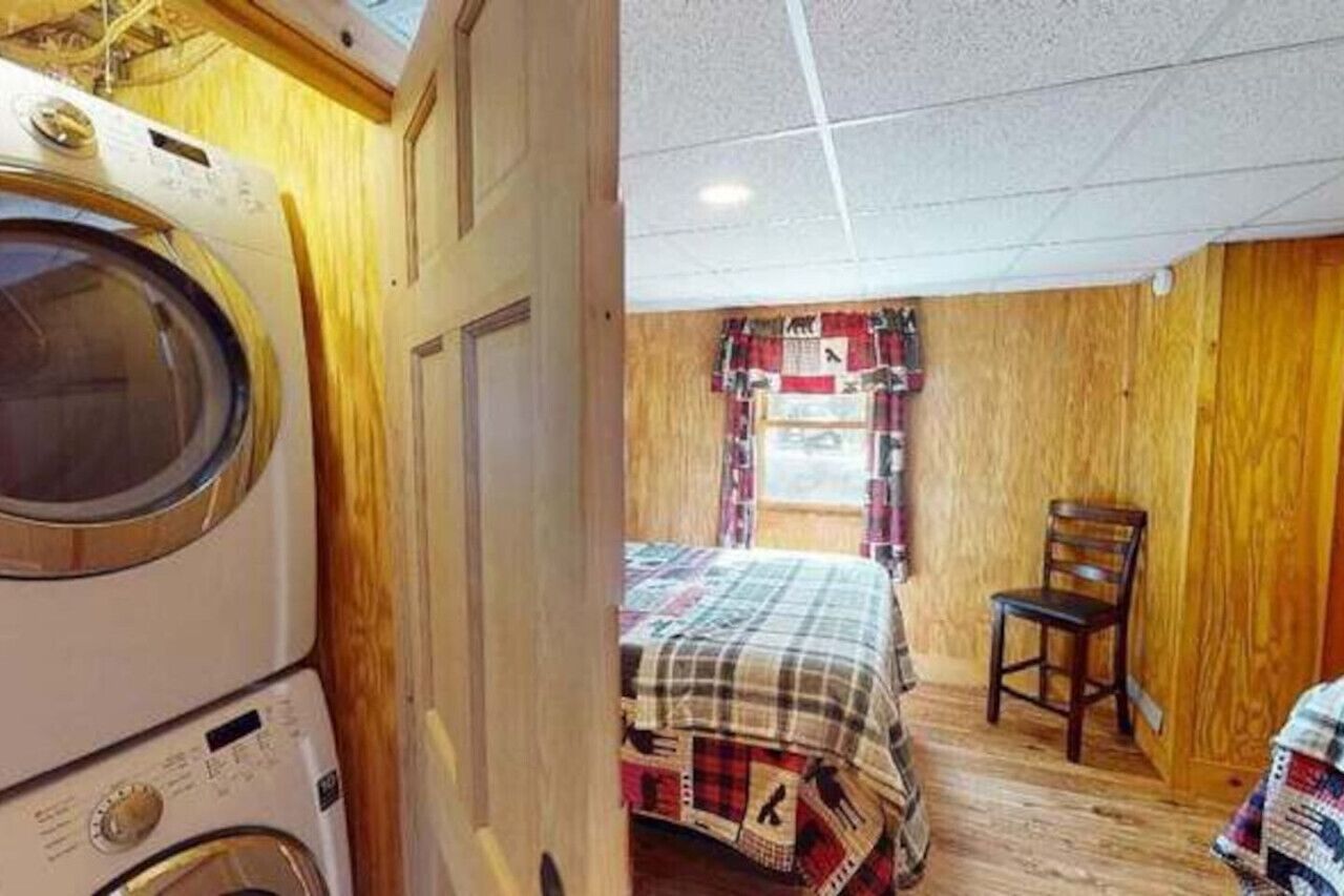 A compact room with a washing machine, a bed with a plaid bedspread, and a wooden chair.