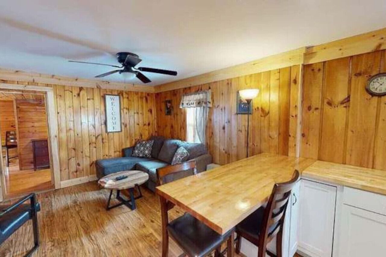 A wooden-paneled room with a sofa, a dining table, and a ceiling fan.