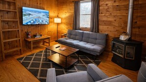 Interior acogedor de una cabaña con sofá, televisión, chimenea y una pared de madera.