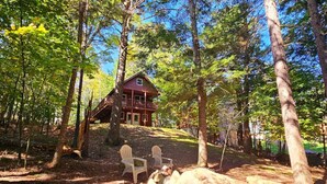 Una cabaña en un bosque con dos sillas Adirondack y un hoyo para la fogata.
