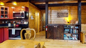 A cozy cabin interior with wooden walls, a kitchen with modern appliances, a dining area, and a bookshelf. - Loon Lodge on Wilson Pond (Greenville)