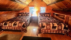 Eine Holzhütte mit zwei Betten, Holzwänden, einer geneigten Decke und einem Fenster.