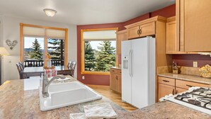 A modern kitchen with granite countertops, a white sink, a refrigerator, and wooden cabinets.
