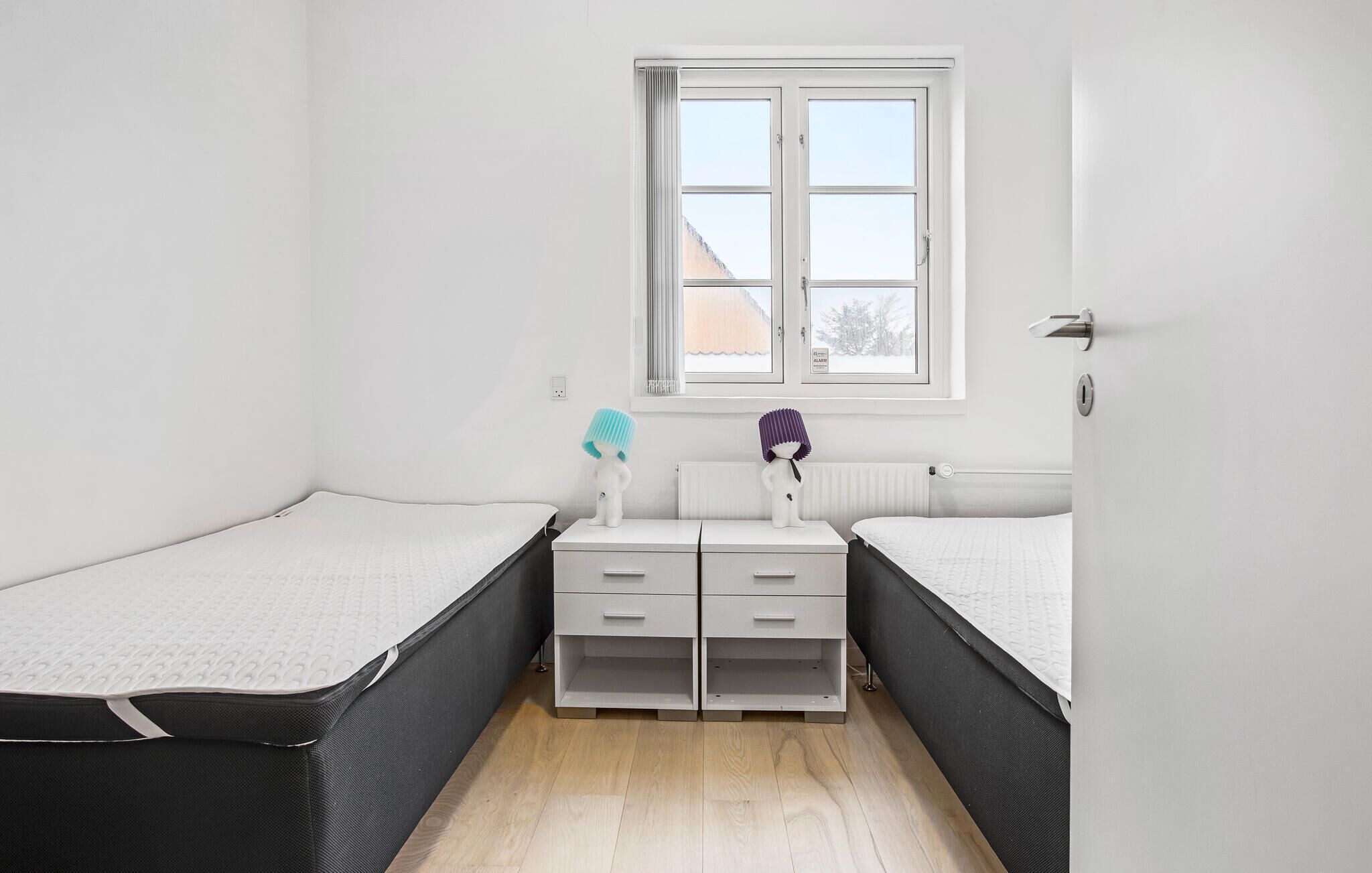 Una habitació petita i lluminosa amb dos llits individuals, una finestra i un radiador.
