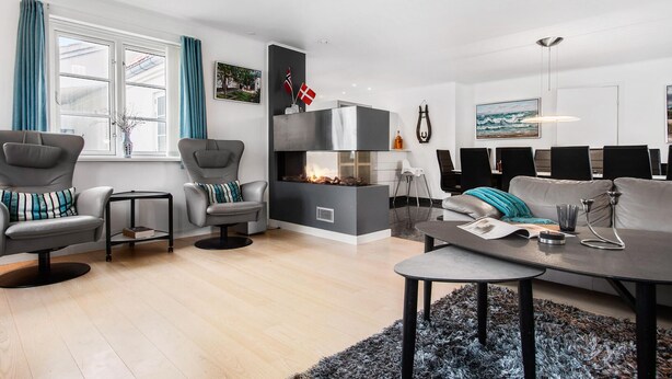 Un salon moderne avec une cheminée, des canapés gris, une table basse et un coin repas comprenant des chaises et une table.