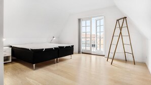 Une chambre avec un lit en mezzanine, une petite table de chevet, une lampe, une fenêtre et une échelle en bois.