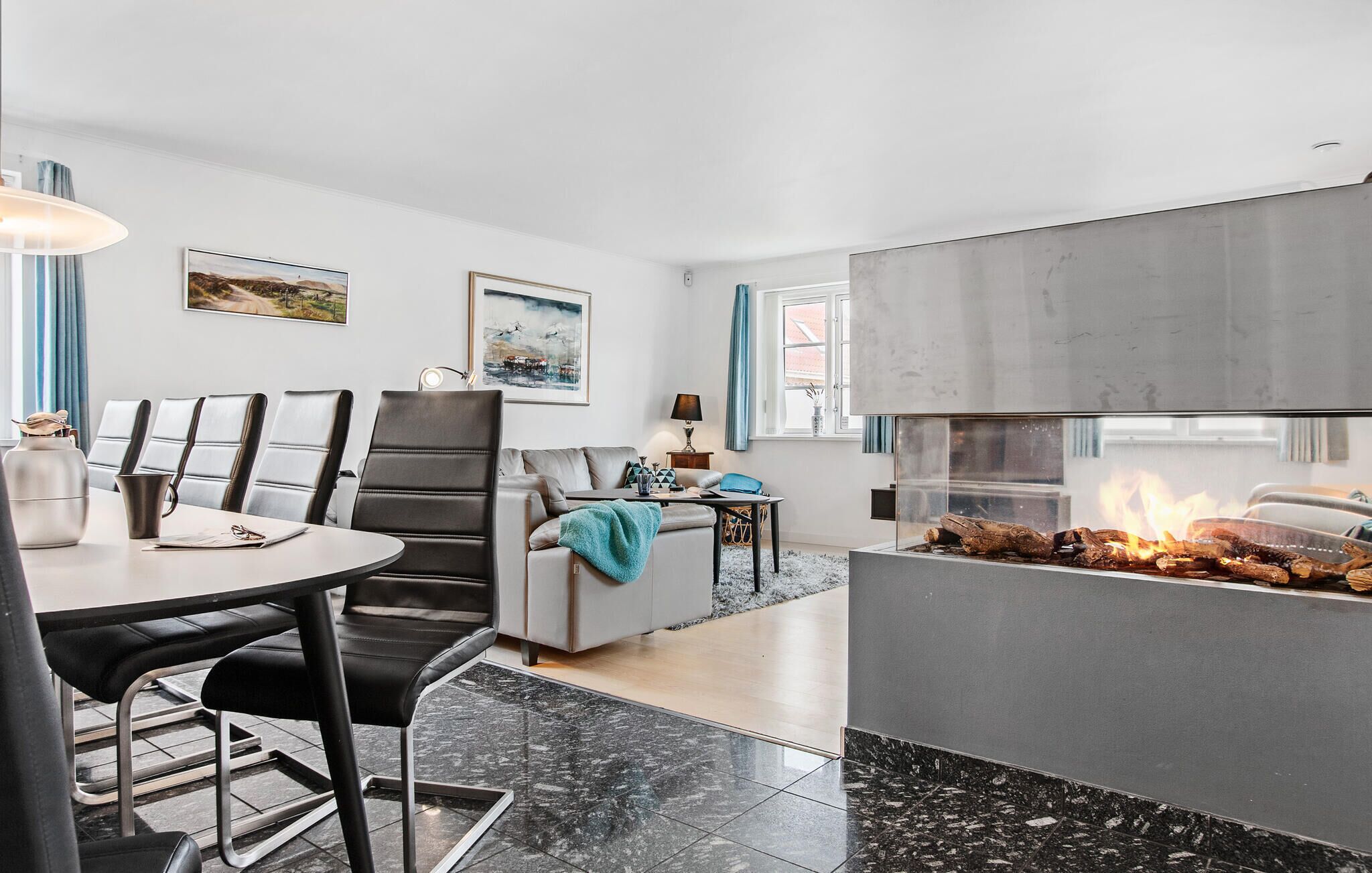 A modern living room with a fireplace, a dining area with a round table and chairs, and a sofa.