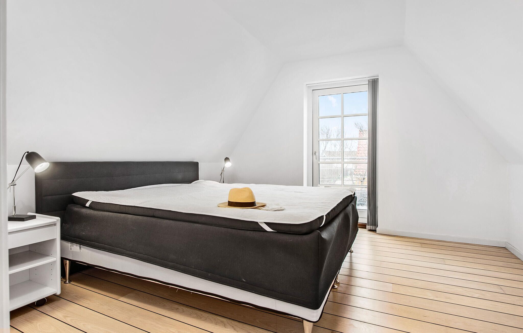 Un dormitorio con cama, mesita de noche, lámpara, ventana y vistas al exterior.