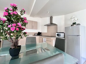 A modern kitchen with a glass dining table, a stainless steel refrigerator, and a microwave.