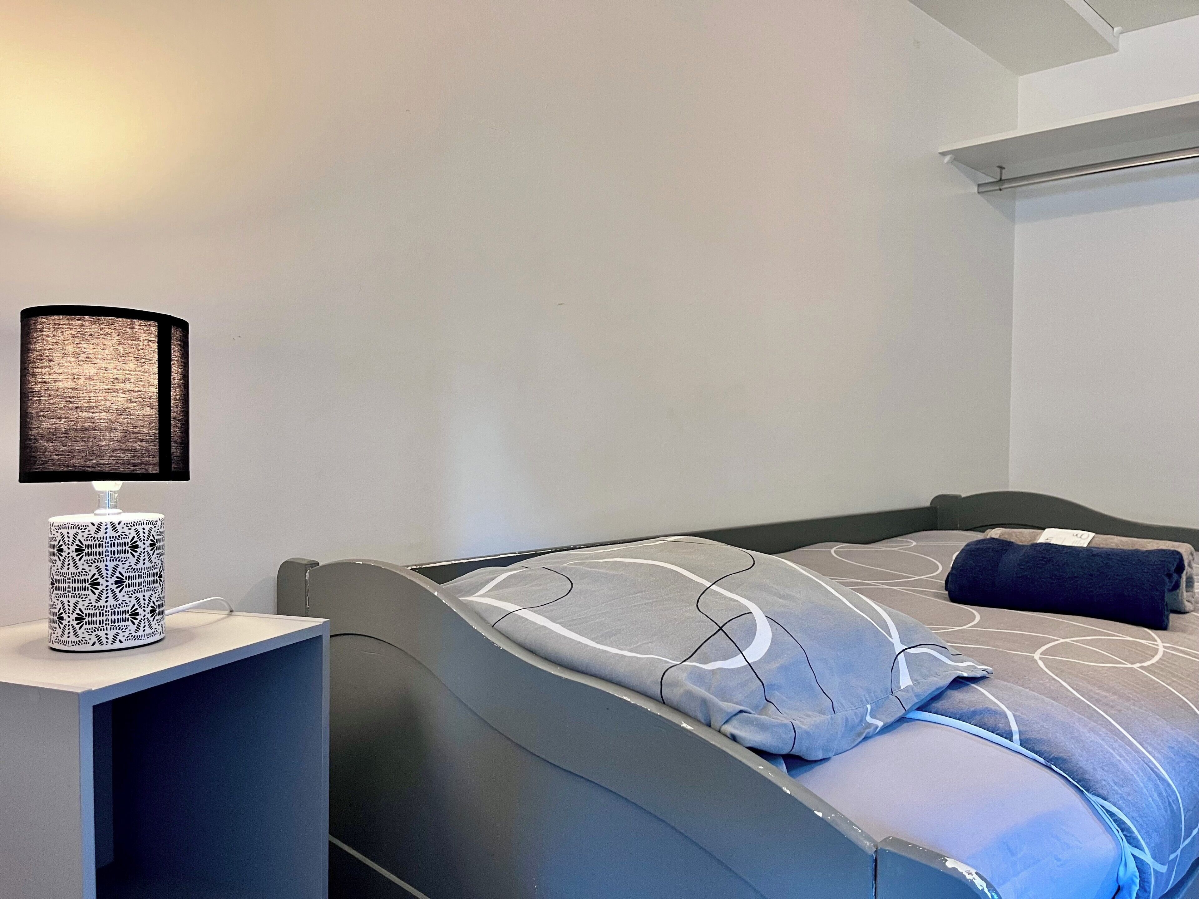 Une chambre à coucher avec un lit, une table de chevet avec une lampe et une étagère fixée au mur.