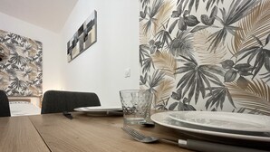 A dining table set with plates, a glass, and cutlery, with a tropical leaf wallpaper and a framed artwork on the wall. - El Castillo - Tournon-sur-Rhône (Tournon-sur-Rhône)