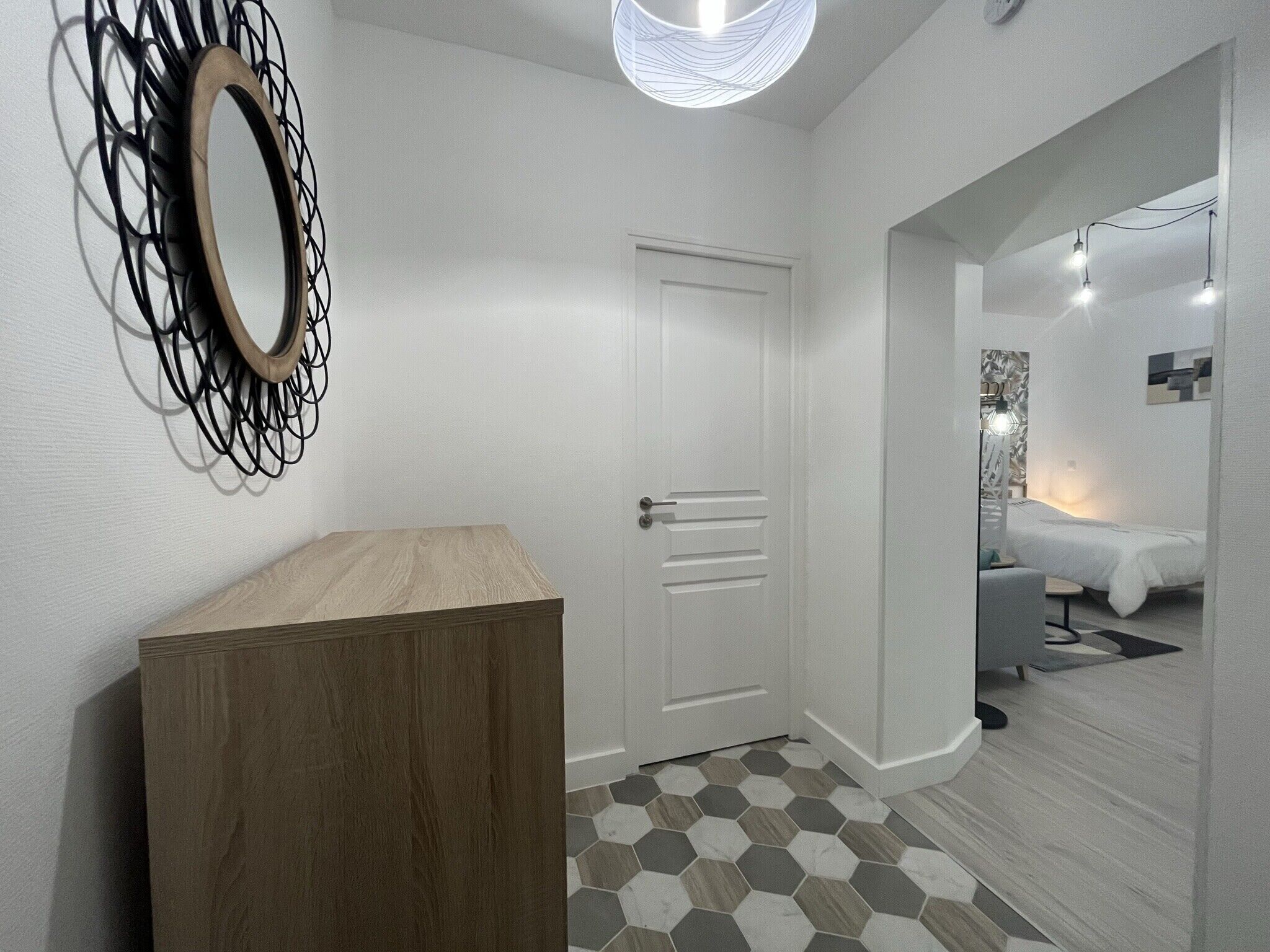 A hallway with a wooden cabinet, a white door, and a room with a bed and a nightstand.