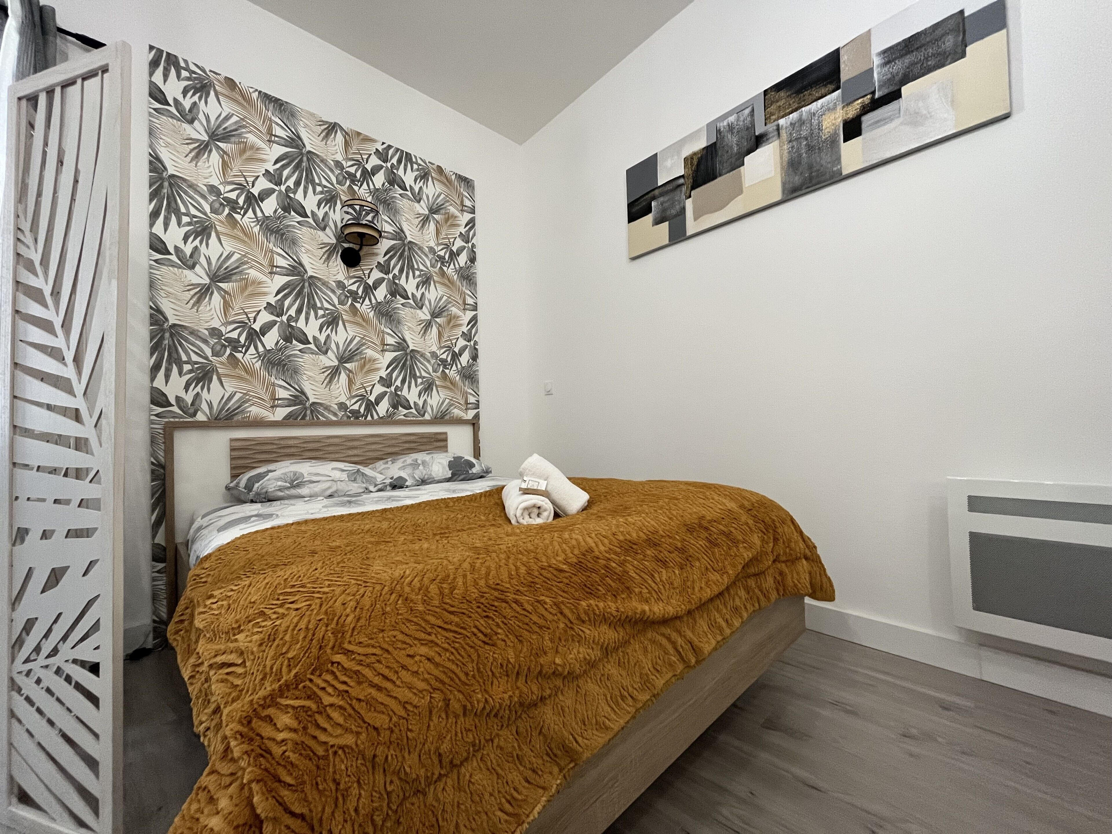 Une chambre à coucher avec un lit, une tête de lit, un mur orné d’un motif de feuilles tropicales et une peinture abstraite moderne.