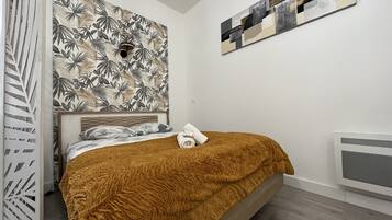 Une chambre à coucher avec un lit, une tête de lit, un mur orné d’un motif de feuilles tropicales et une peinture abstraite moderne.