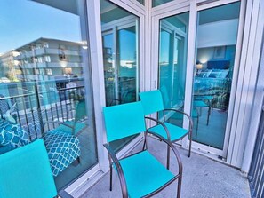 Ein Balkon mit Glastüren, türkisfarbenen Stühlen und einem gemusterten Kissen.