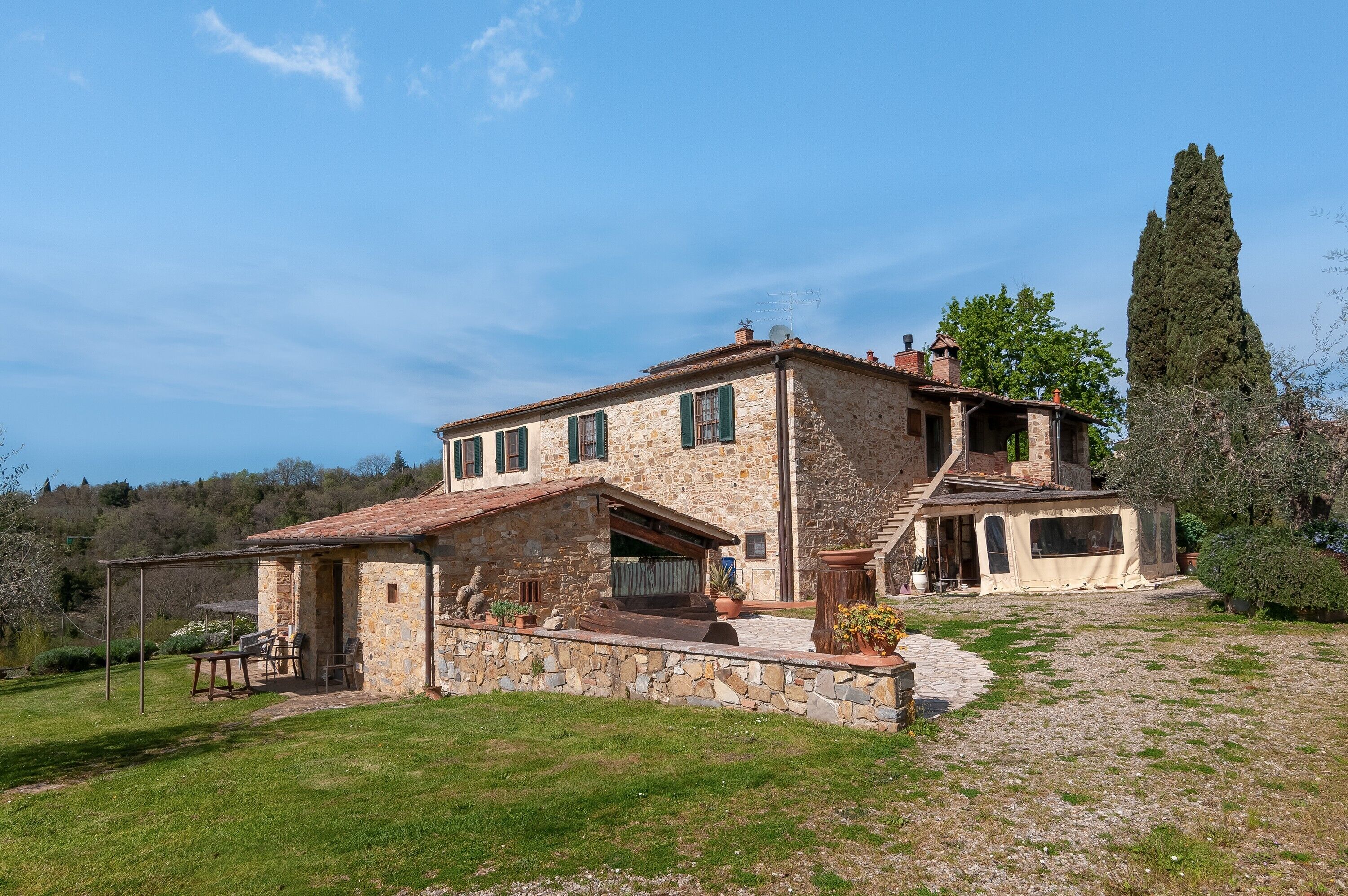 A stone house with a patio, outdoor seating, and a large tree.
