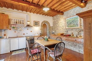 A rustic kitchen with a stone wall, wooden ceiling, and a dining table with chairs.