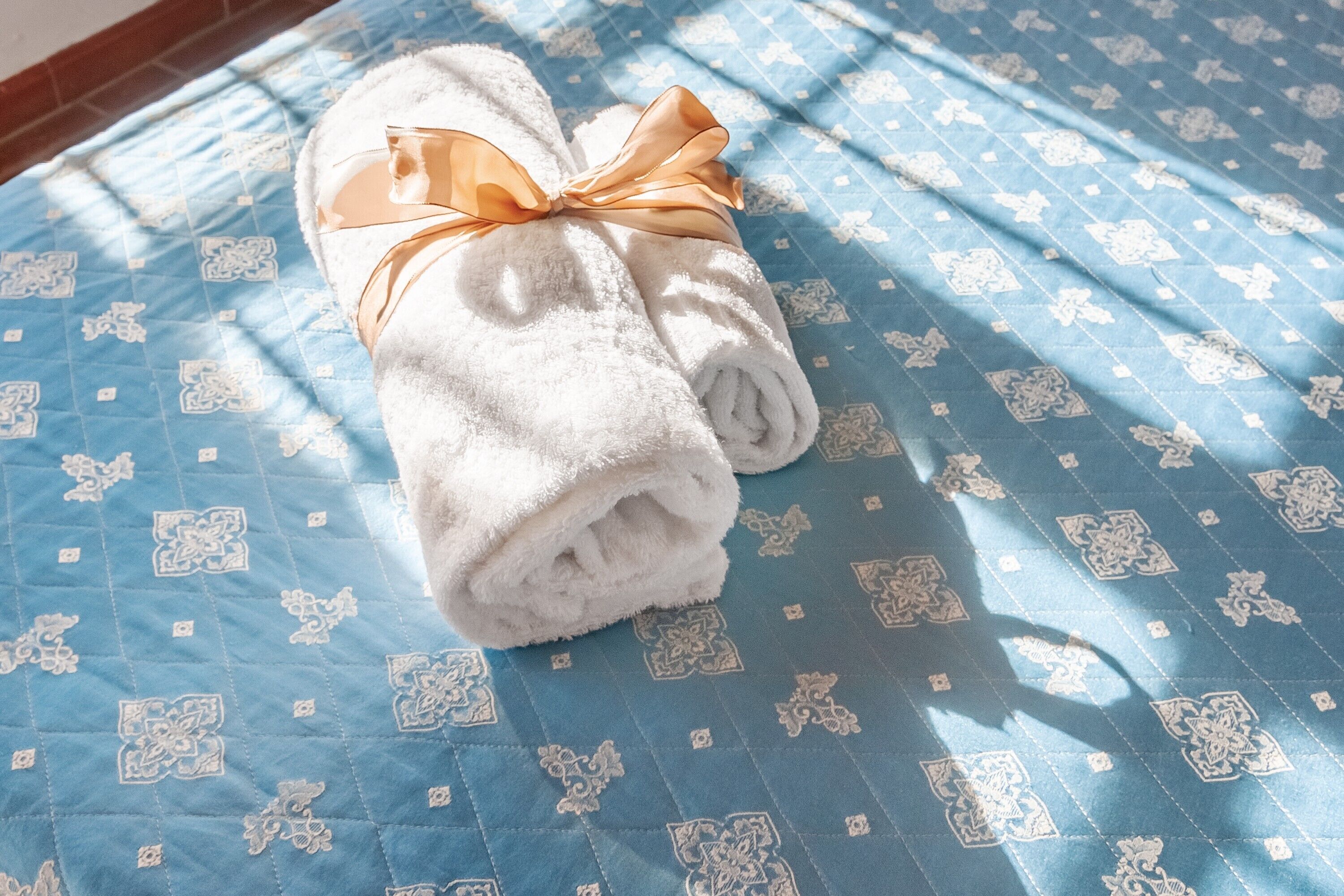 Ein gefaltetes weißes Handtuch mit Schleife auf einer blauen, gemusterten Bettdecke.