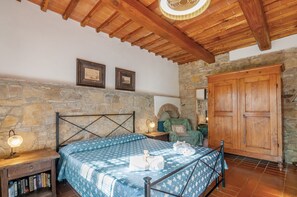 A bedroom with a stone wall, wooden ceiling beams, a bed with a patterned bedspread, a nightstand with a lamp, and a wooden wardrobe. - Agriturismo 'Molinuzzo - Joshua' with shared pool, private terrace and Wi-Fi (Barberino Tavarnelle)