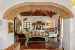 Un plafond voûté en briques, une cheminée, un canapé et un lit dans une pièce dont le sol est recouvert de planches de bois.