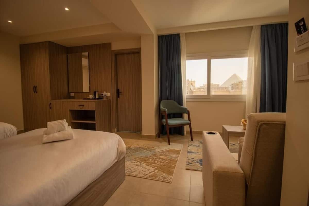 A hotel room with a bed, a desk, a chair, and a view of a pyramid through the window.