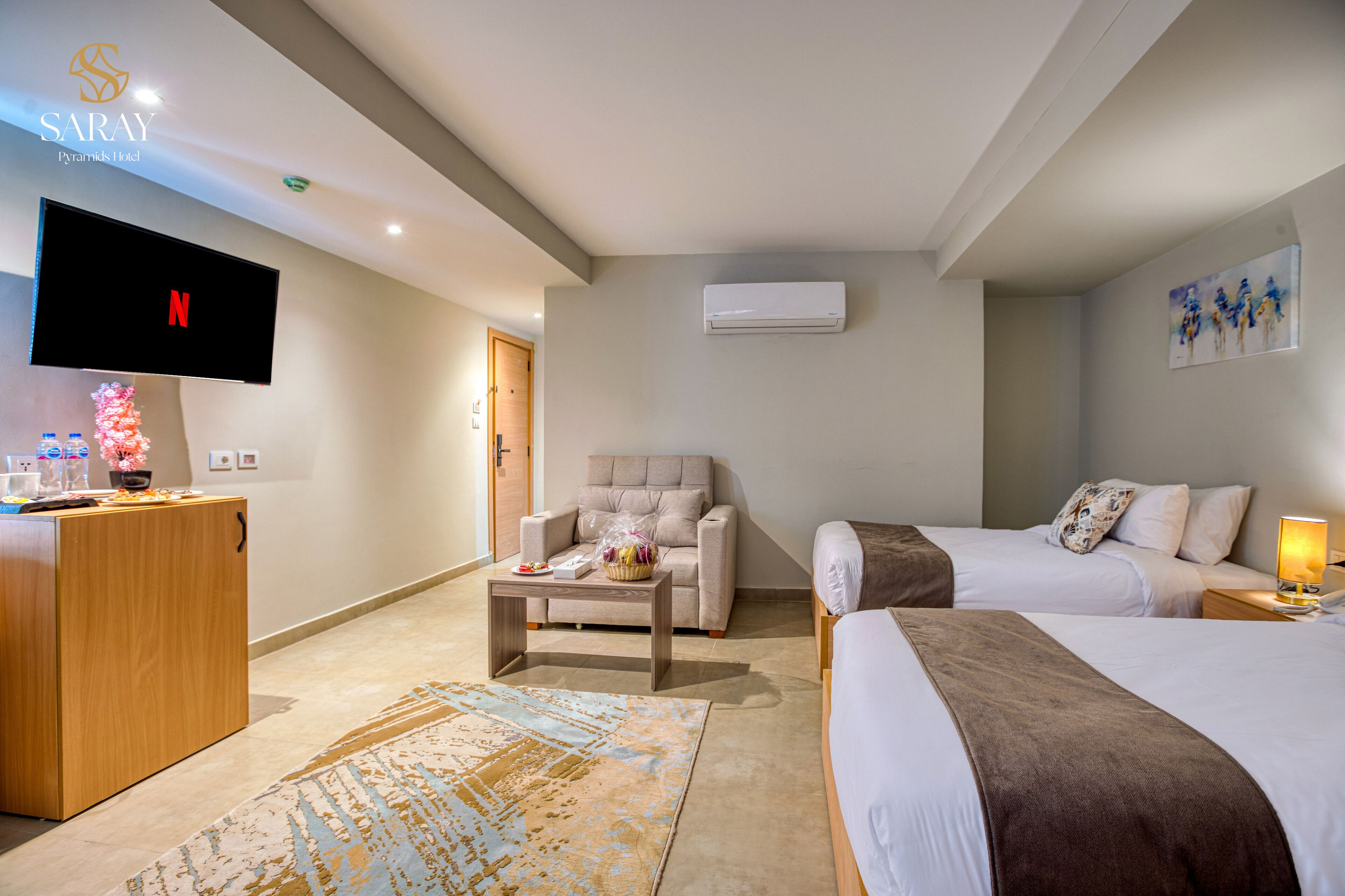 Habitación de hotel con televisor de pantalla plana, sofá, dos camas, una mesa de centro y una planta decorativa.