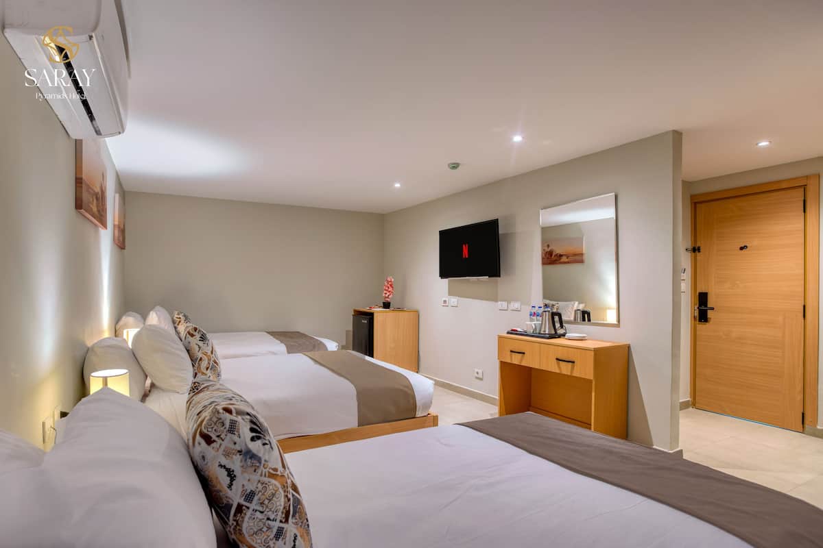 A hotel room with two beds, a desk, a TV, and a wooden door.