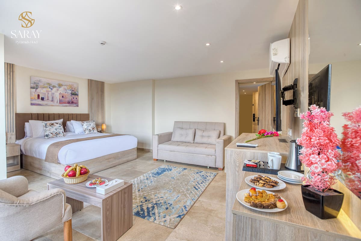 A modern hotel room with a bed, a sofa, a desk with a vase of flowers, and a breakfast tray.