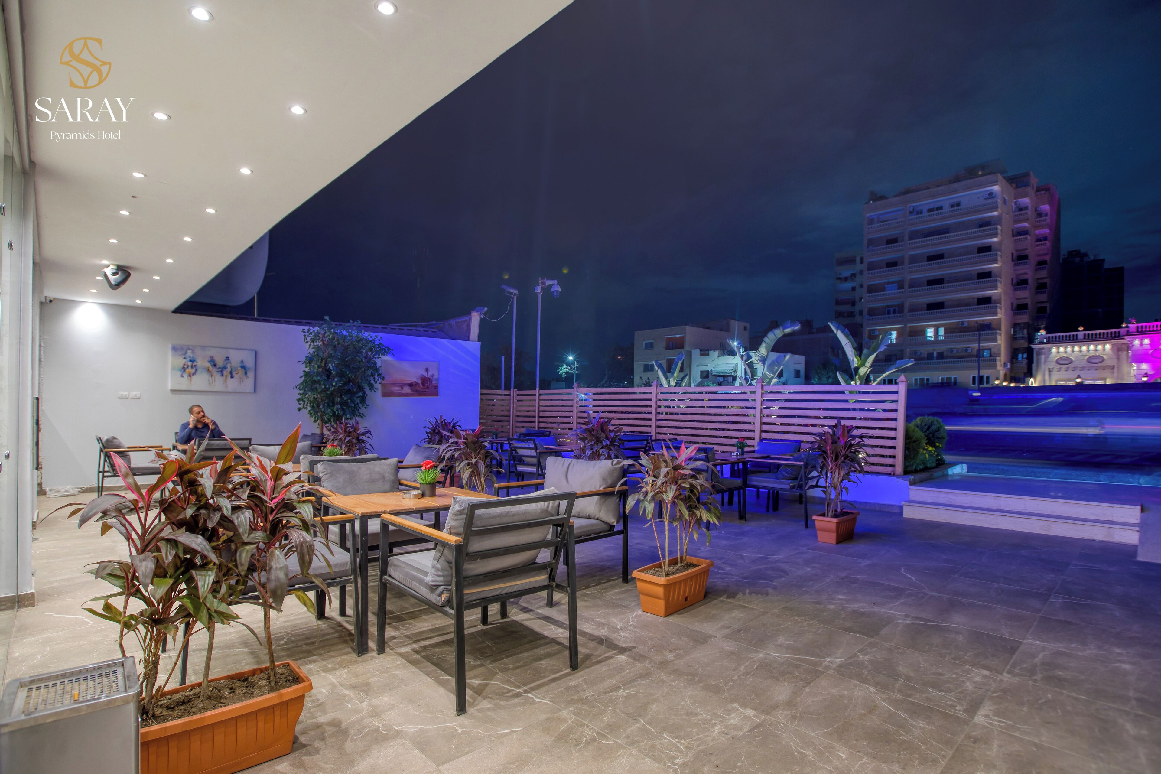Una terrazza sul tetto con posti a sedere, piante in vaso e vista sulla città illuminata di notte.