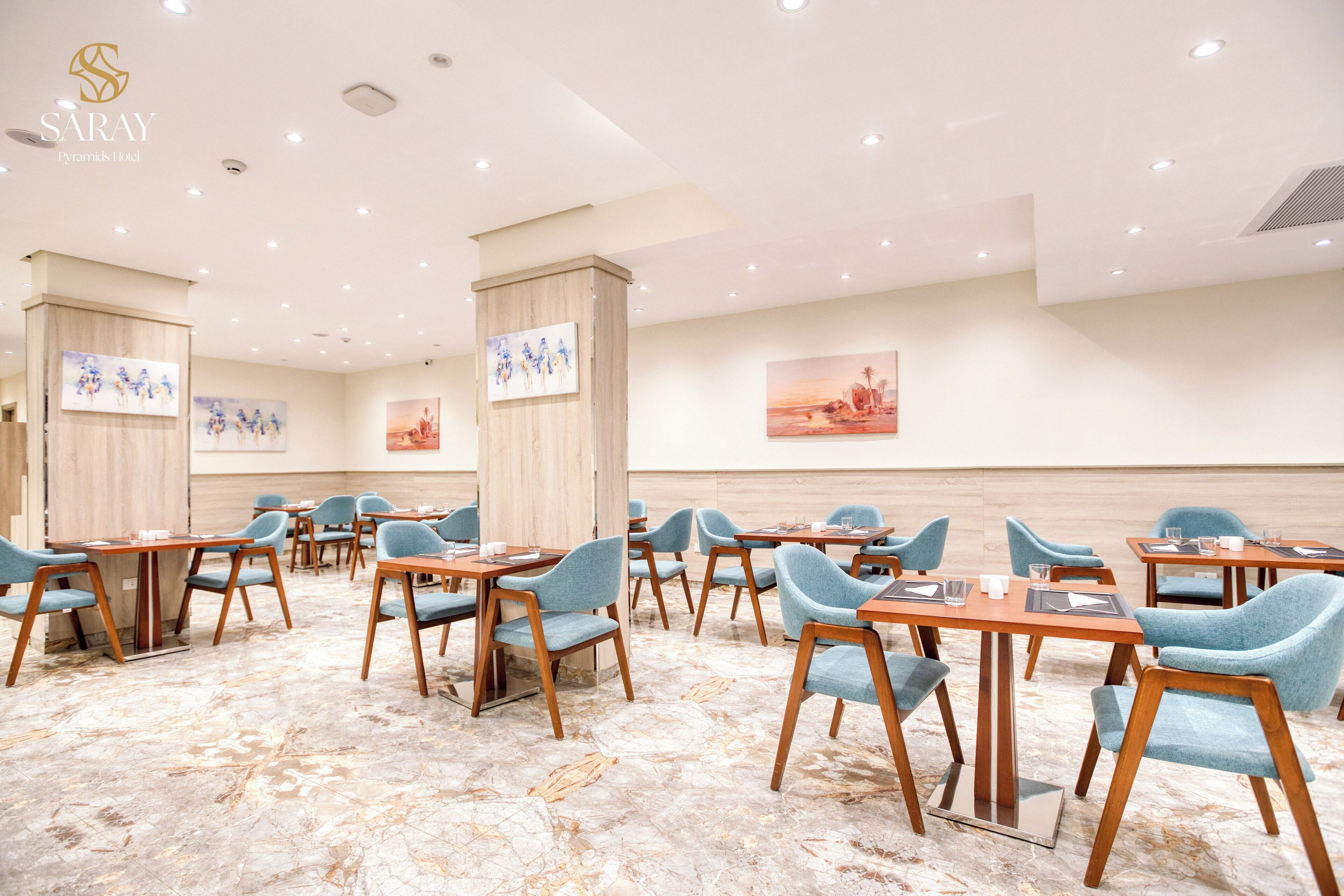 A hotel conference room with wooden tables and blue chairs, marble flooring, and artwork on the walls.