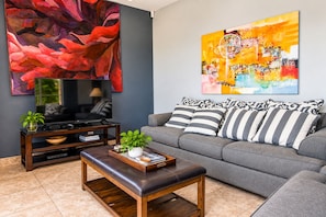 A modern living room with a grey sofa, striped pillows, a wooden coffee table, a TV on a stand, and two abstract paintings.