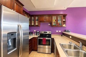 A modern kitchen with stainless steel appliances, wooden cabinets, and a purple wall.